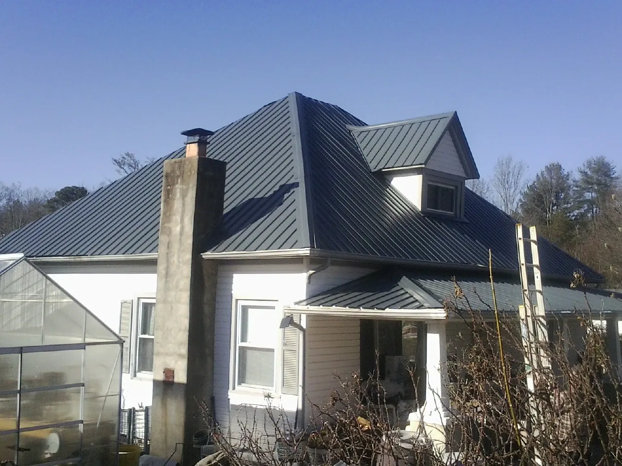 Dark blue standing seam metal roof on a white farmhouse with dormer — Slate & Tile Roof Repair by Roofing Brothers in Glen Head