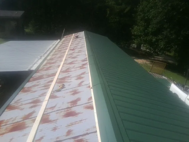Old rusted panels beside newly installed green metal roofing — Wind Damage Roof Repair by Roofing Brothers in Glen Head