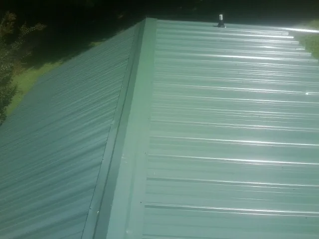 New green metal panels meeting at the ridge of a roof — Flat Roof Repair work by our crew in Glen Head