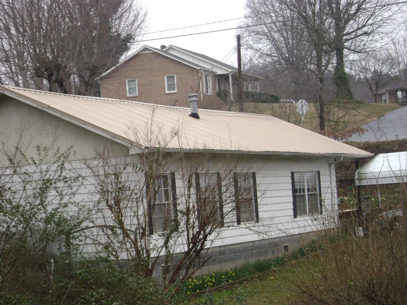 Tan metal roof on a white sided house set into a hillside — Commercial Roofing by Roofing Brothers in Glen Head