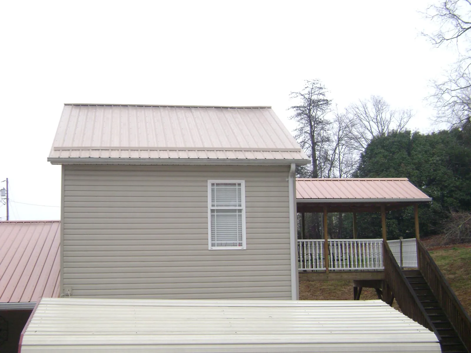 Tan metal roofs on a two story addition and attached porch, from a Roof Replacement job in Glen Head
