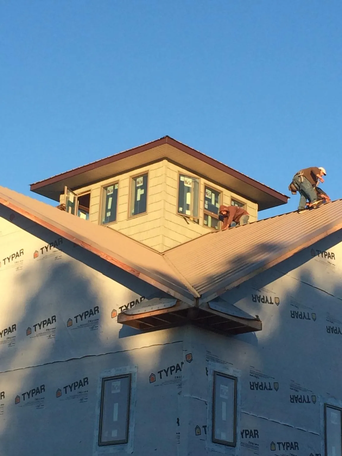 Roofers working around a rooftop cupola on a new metal roof at sunset — Roof Waterproofing in Glen Head by Roofing Brothers